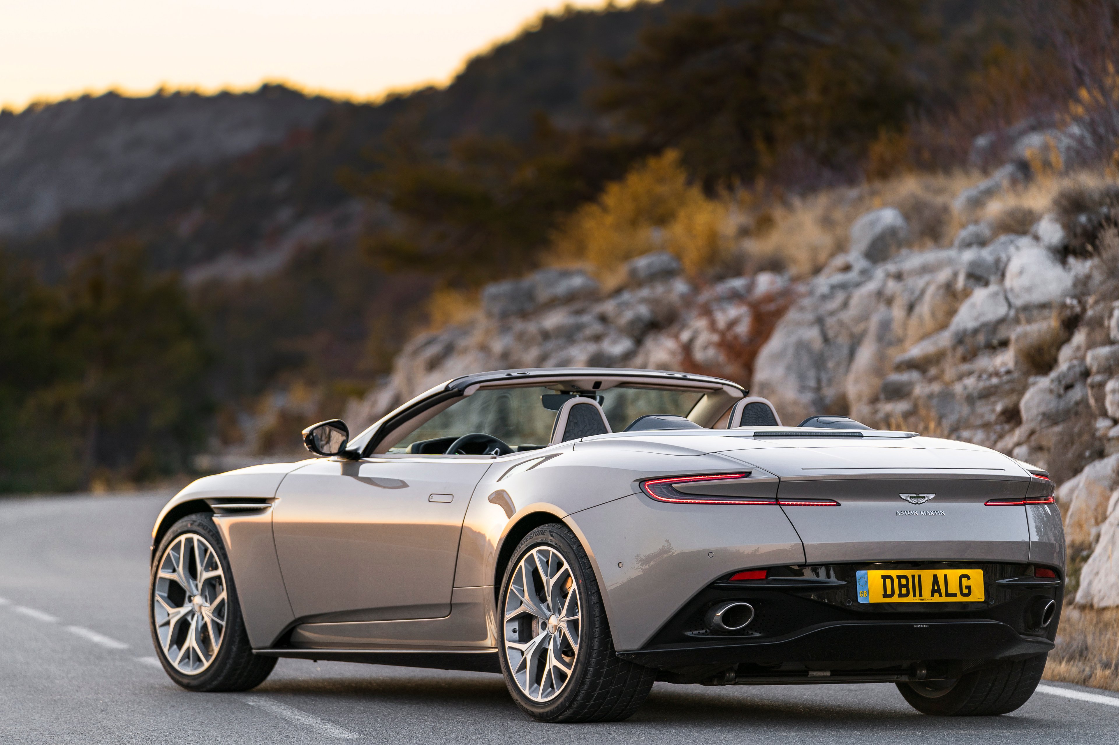 A silver Aston Martin DB11 Volante, a sleek luxury-sports convertible, shown from a rear three-quarter view.