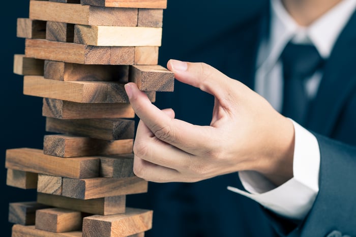 A person in a suit carefully pulling a block out of a block tower.