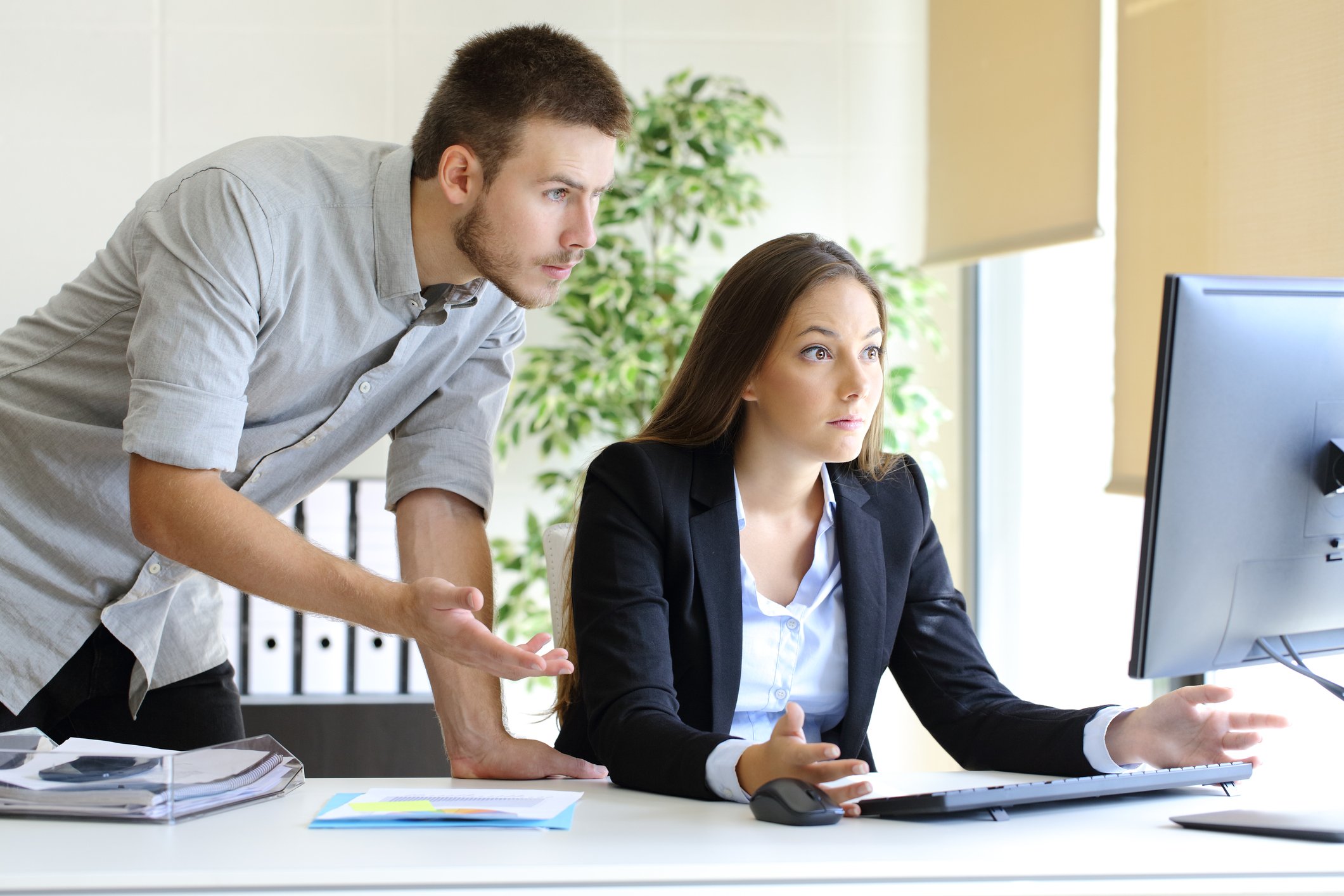 Two young businesspeople shrugging and staring over a computer screen.