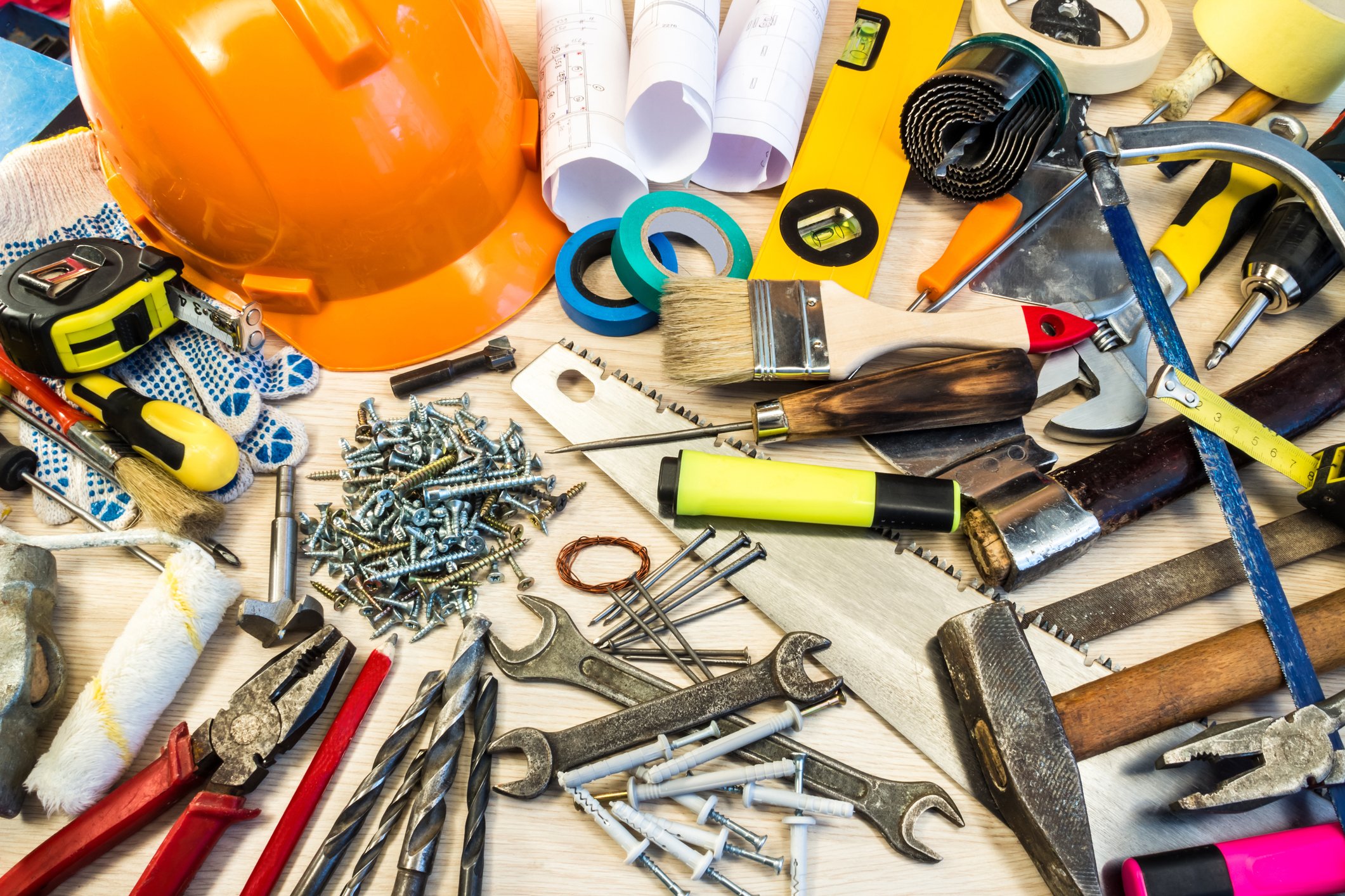 Several hand, power, and construction tools and tapes scattered on a table.