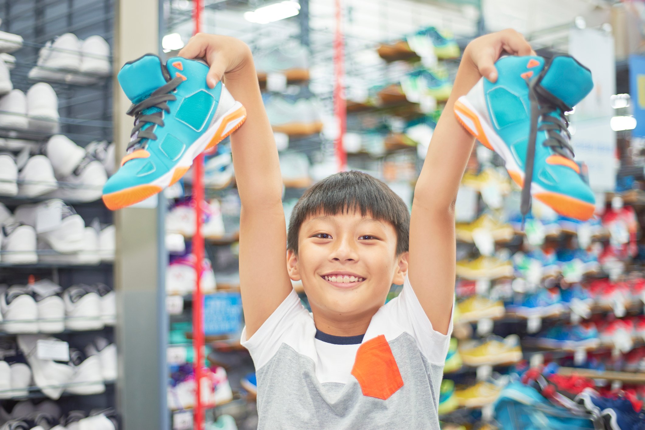 A young boy holds up a pair of sneakers.