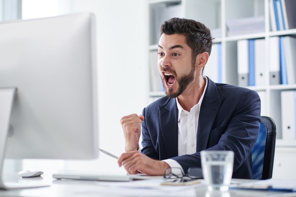 Happy young man screaming of joy when looking at computer screen