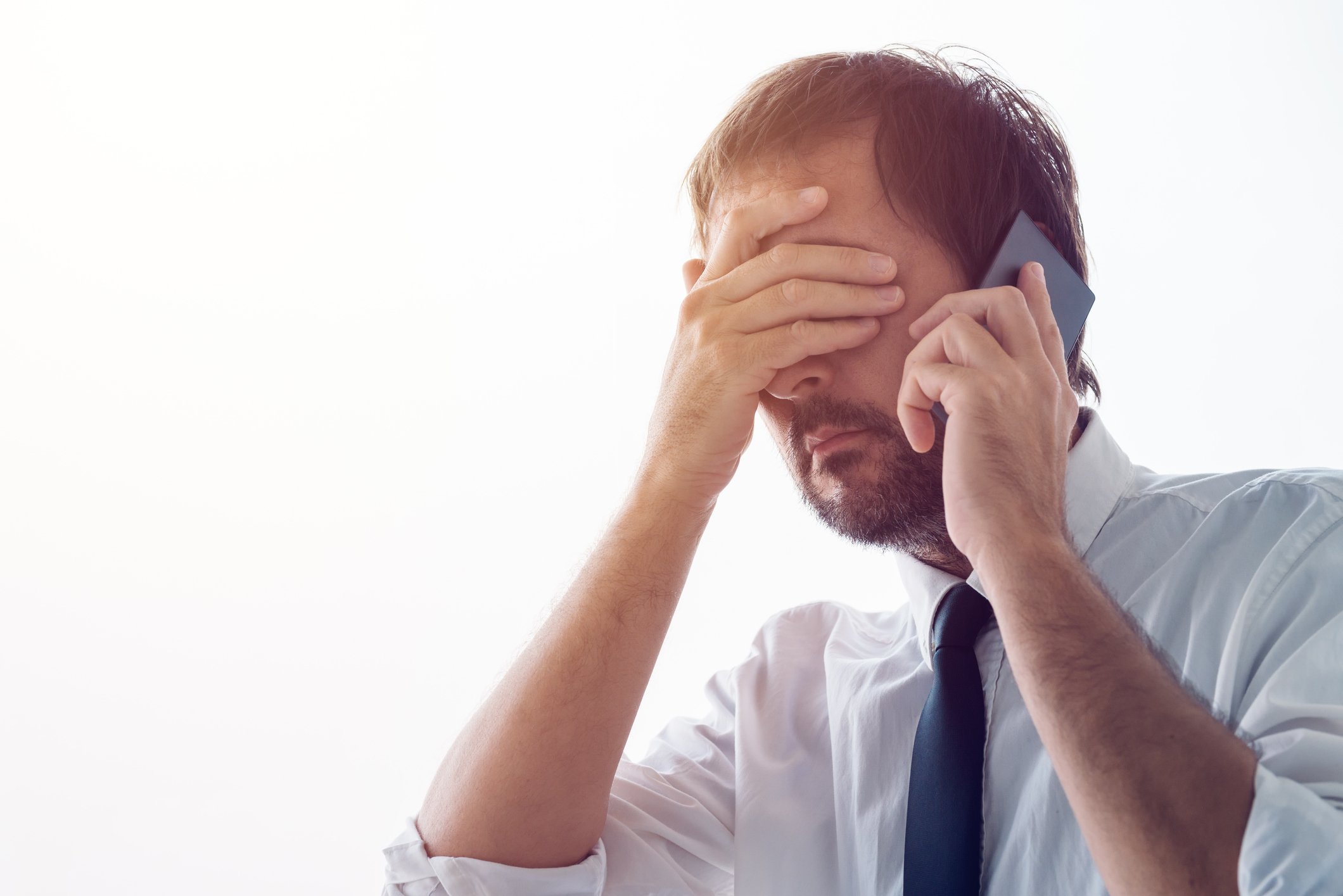 A person in a suit with their hand over their face talking on phone.