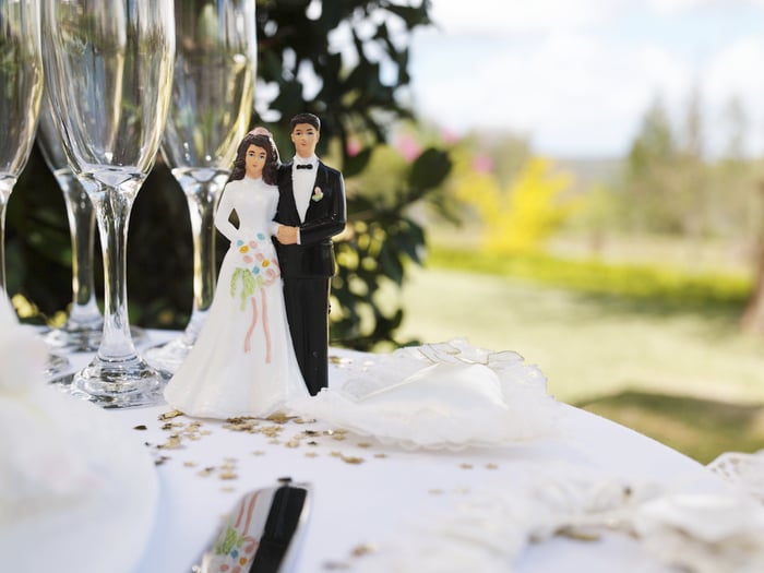 Wedding couple figurine on table with champagne flutes in front of an outside venue.