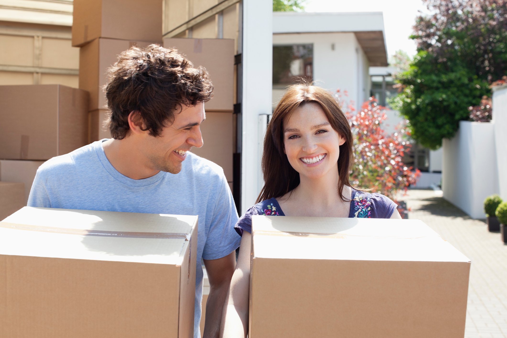 A young adult male and female carrying boxes from a truck parked in front of a home.