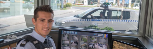 Security guard in glass office with Brink's car outside.