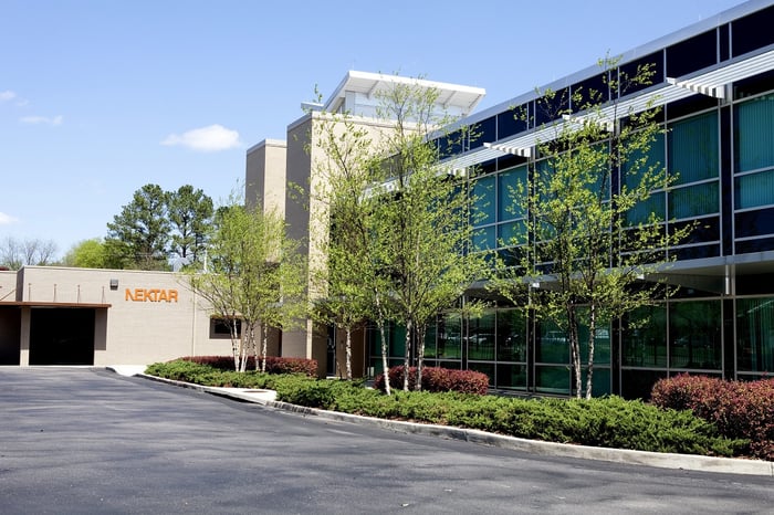 Two-story glass office building, parking lot, and one-story entry building with Nektar logo on it.