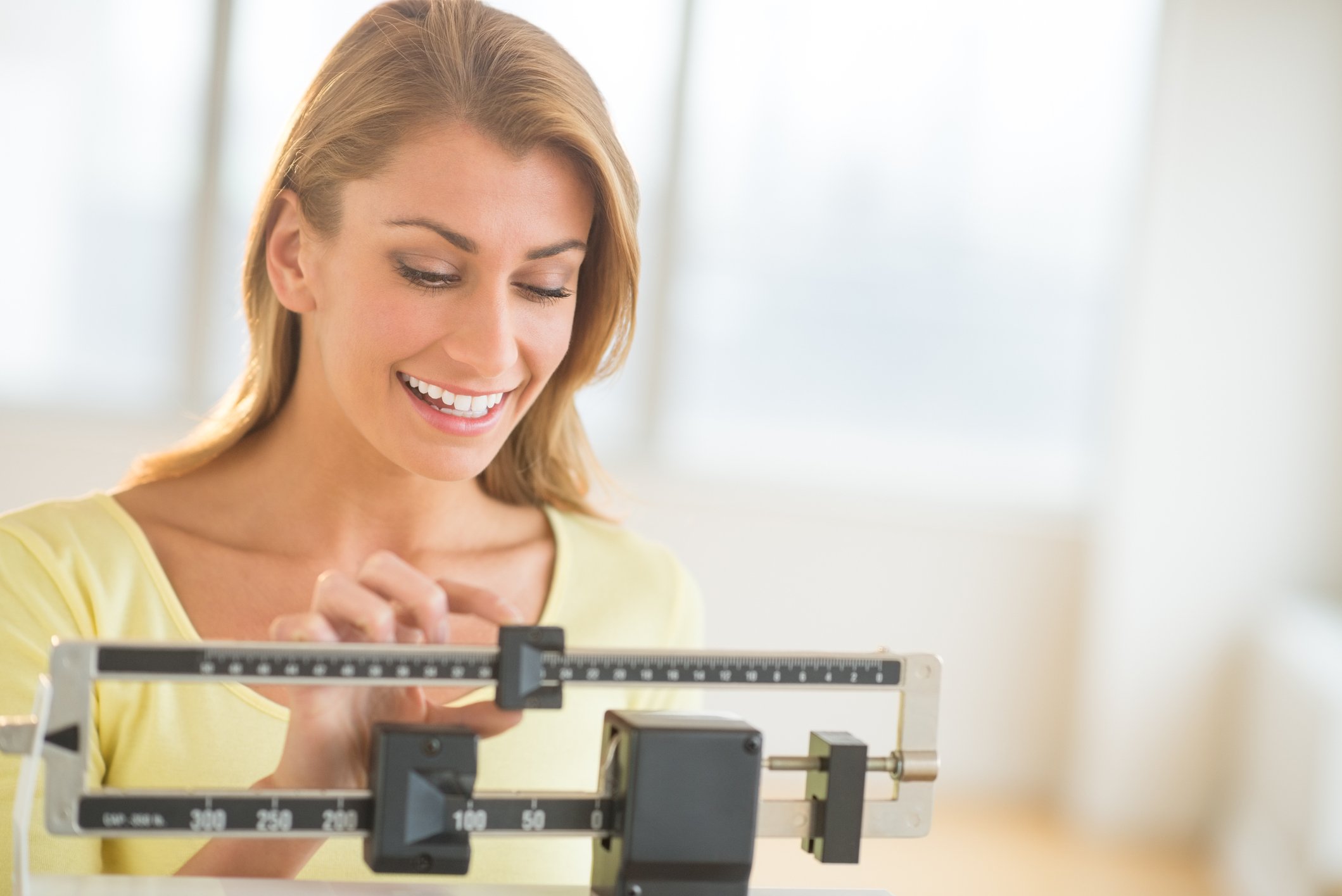A smiling woman weighing herself on a balance scale.