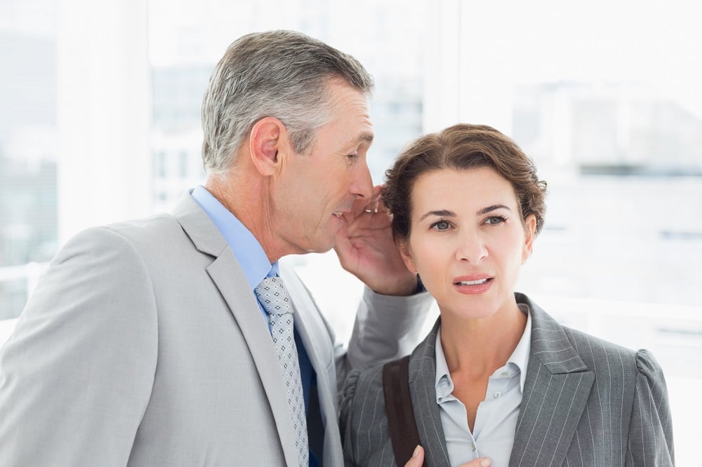 A businessman whispers into a businesswoman's ear.