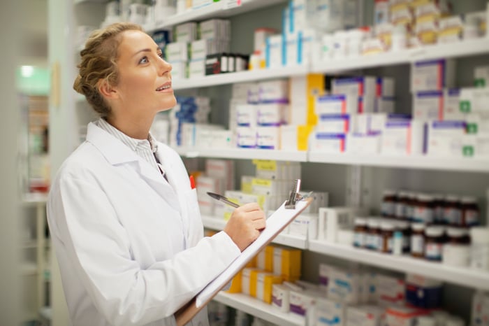 A female pharmacist with a clipboard looking at shelves of medicine.
