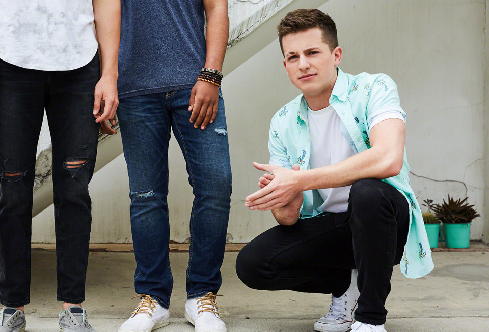 A young man squatting beside two others who are standing.