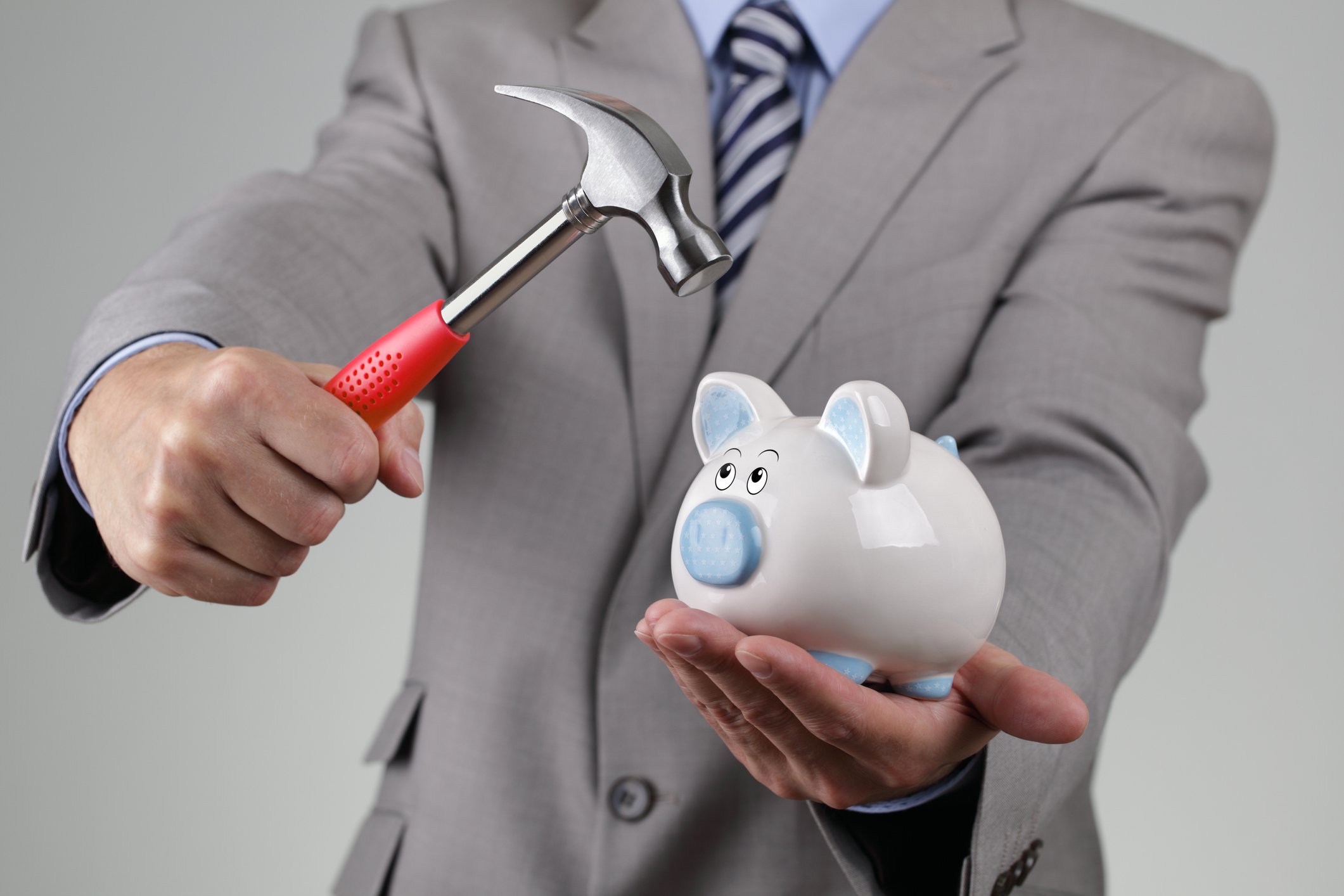 Man in suit holding a hammer aimed toward a piggy bank
