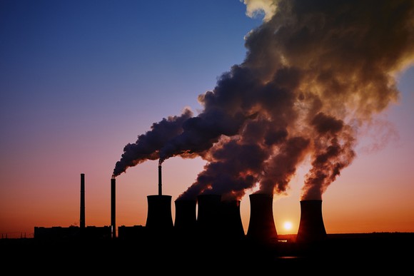 Steam rising from the cooling towers of a coal-fired power plant in silhouette. 