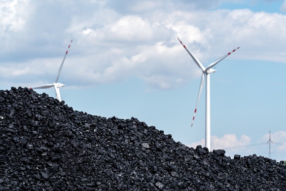 A pile of coal in the foreground, with several wind turbines in the background.