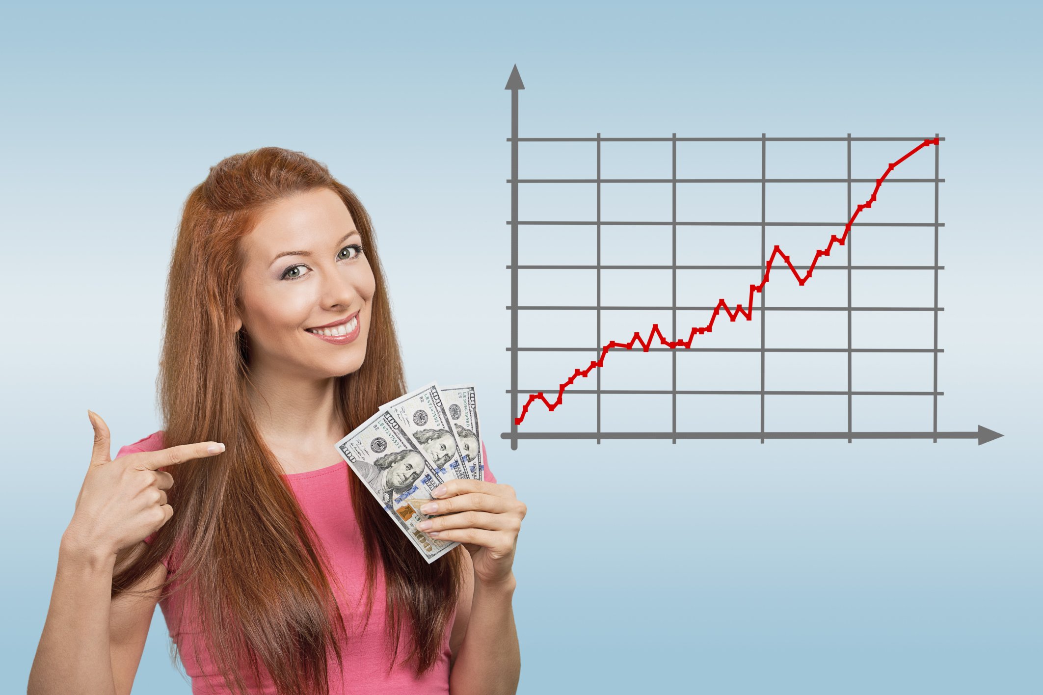 A young woman pointing to, and holding, a fanned pile of hundred dollar bills, next to a rising stock chart.
