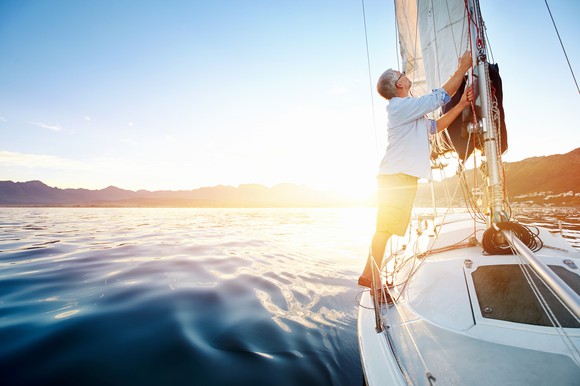 Man fixing the sail on a sailboat that's on open waters.