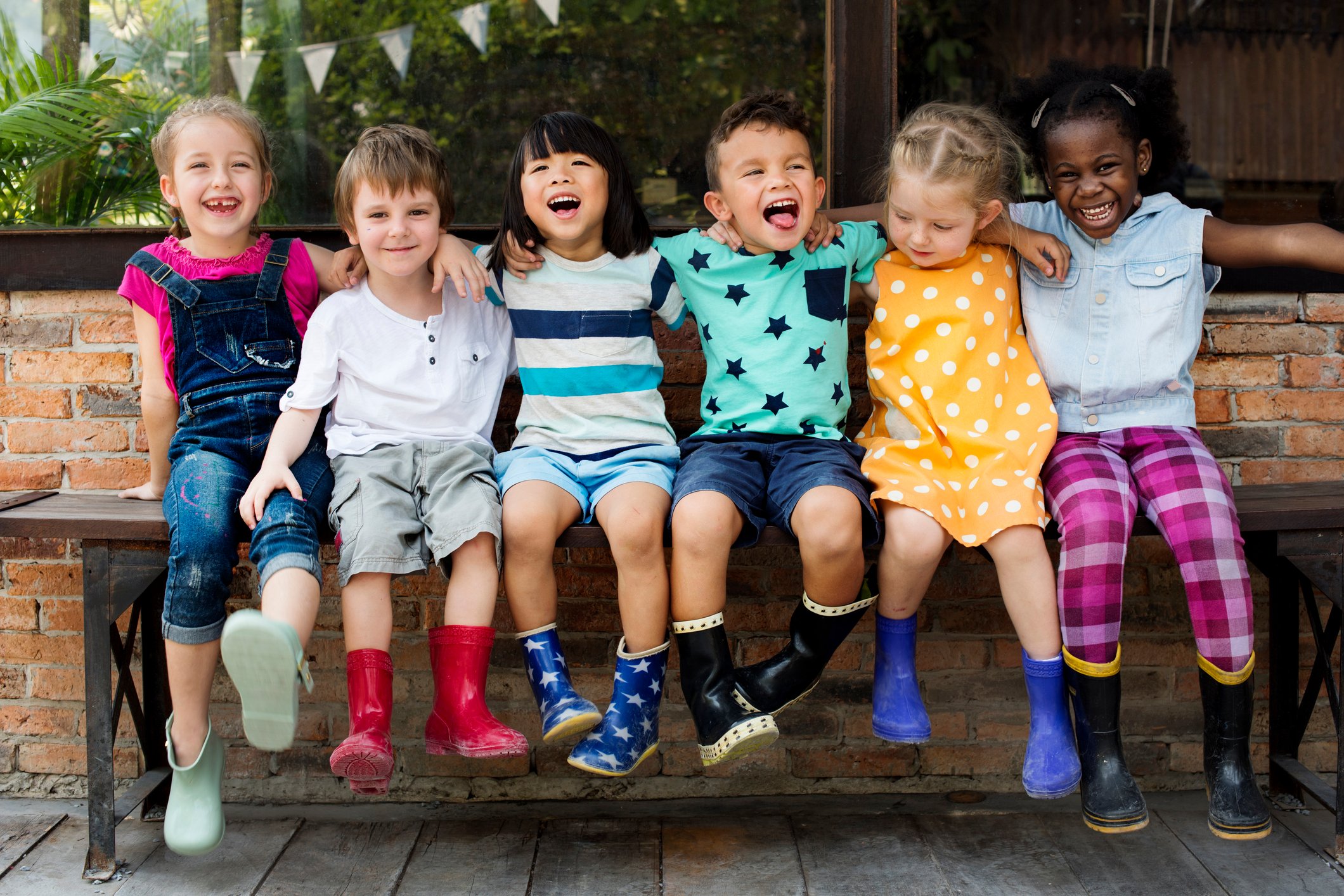 Six kids sitting on a bench smiling and laughing.