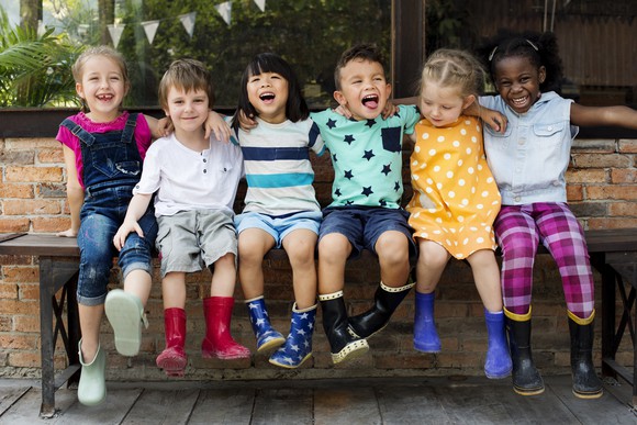 Six kids sitting on a bench smiling and laughing.