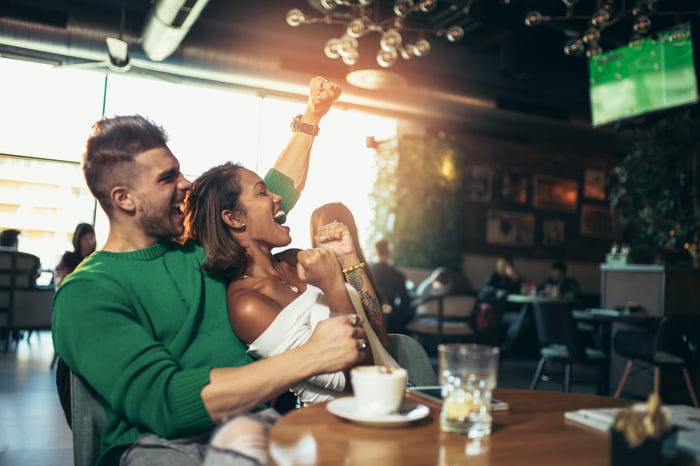 A couple cheering while watching a game on television in a sports bar