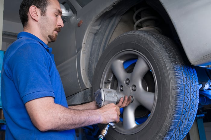 A mechanic changing a tire on a car that's up on a lift.