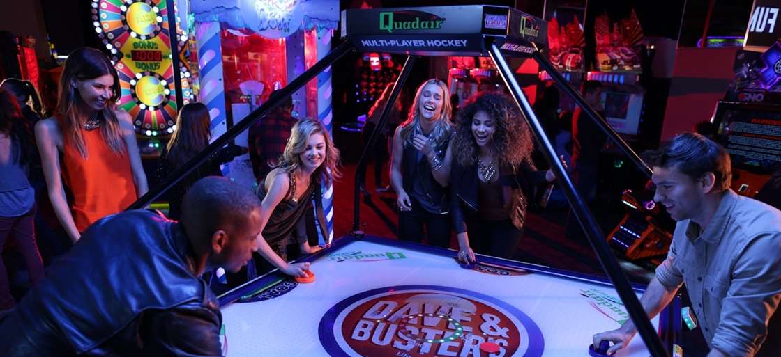 a group of young people playing a type of air hockey at a Dave & Buster's.