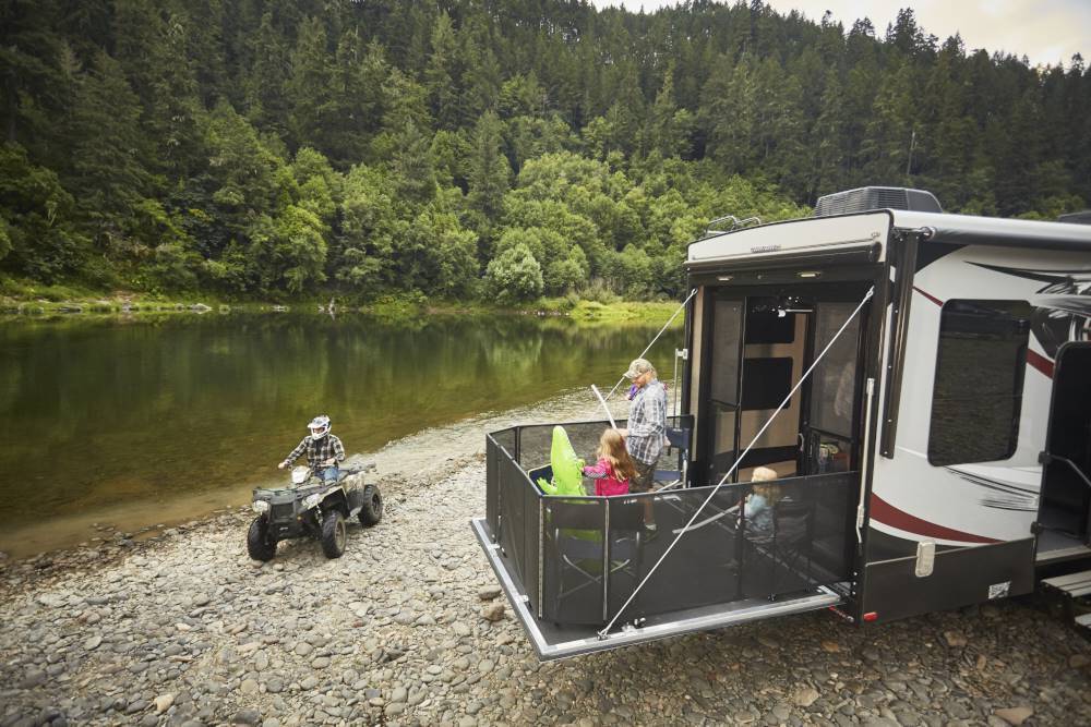 Family enjoying activities on camper parked by a riverside.