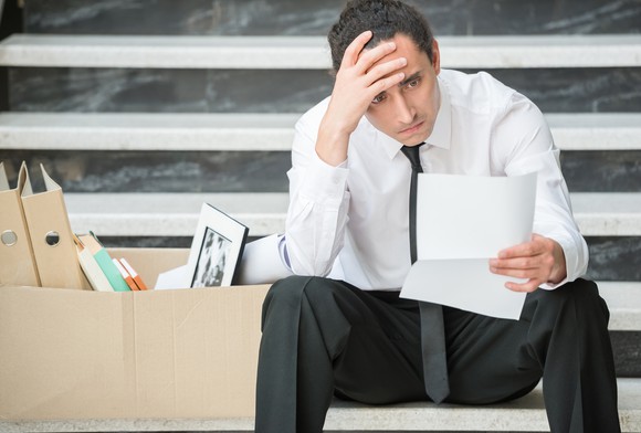 Man holding his head with a document in hand, with a box of office supplies next to him