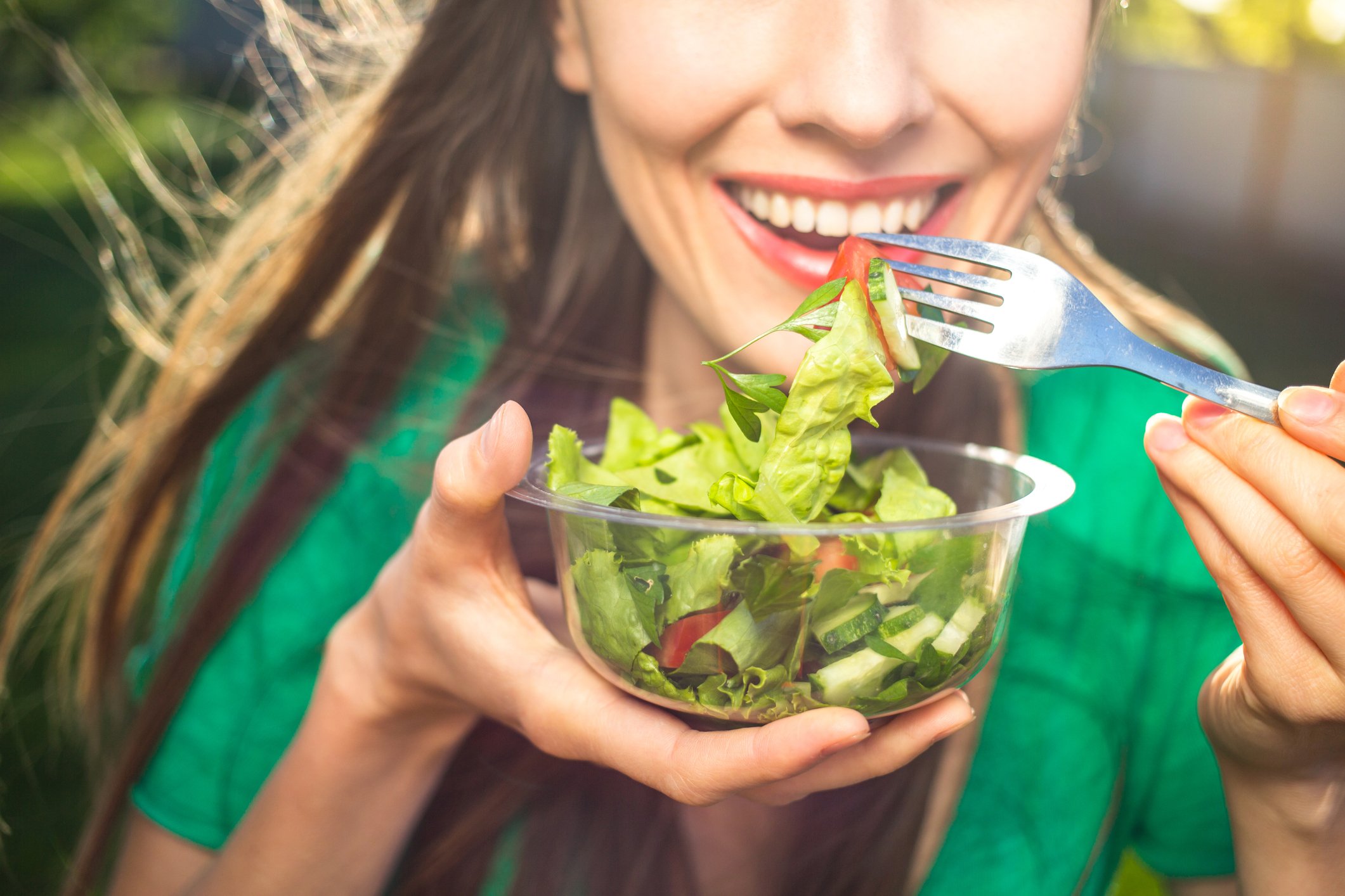 Close-up of woman eating green salad with a fork from a glass bowl.