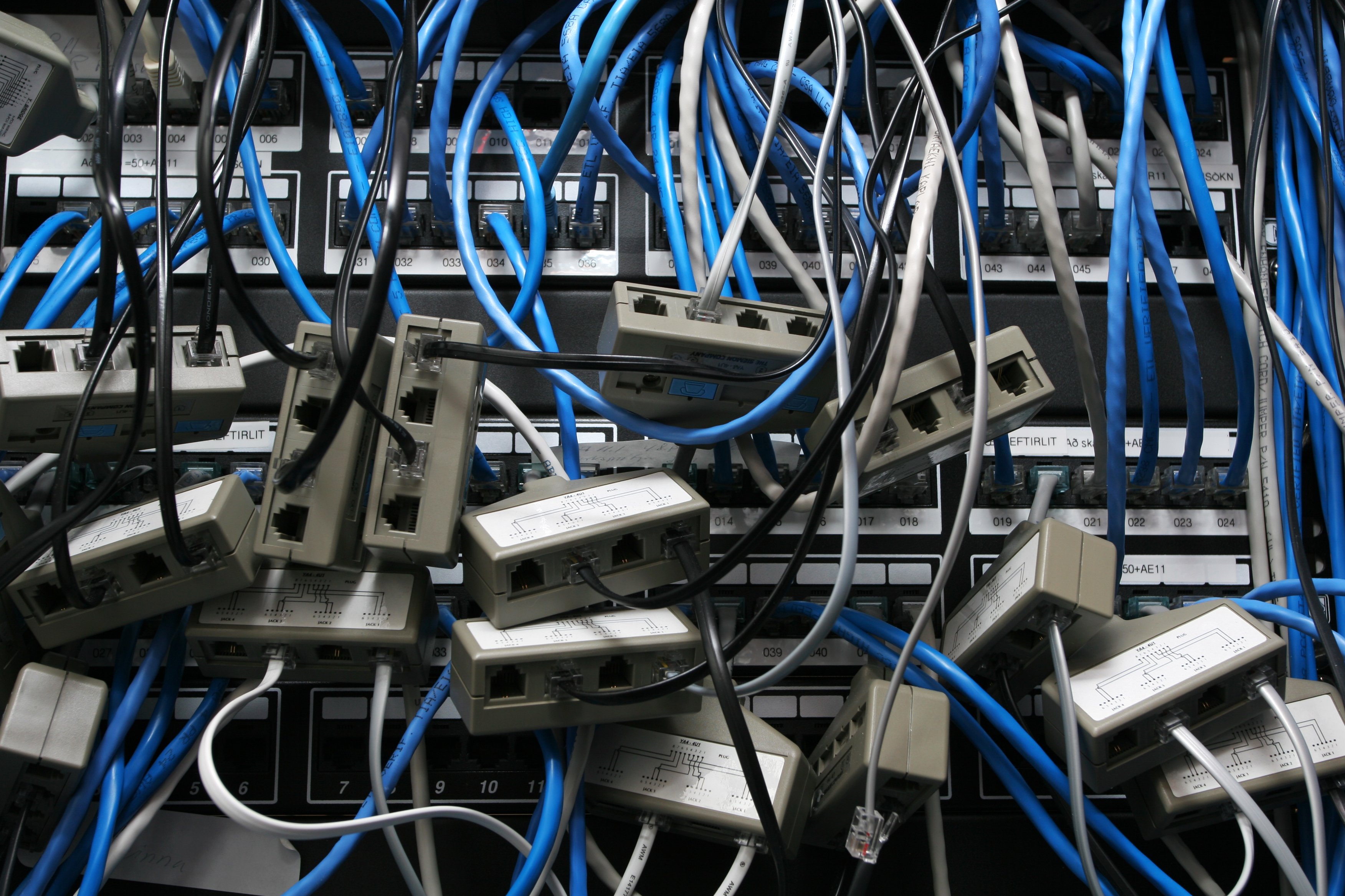 A rack of networking routers and switches, populated by a jumble of blue Ethernet cables and random adapters.