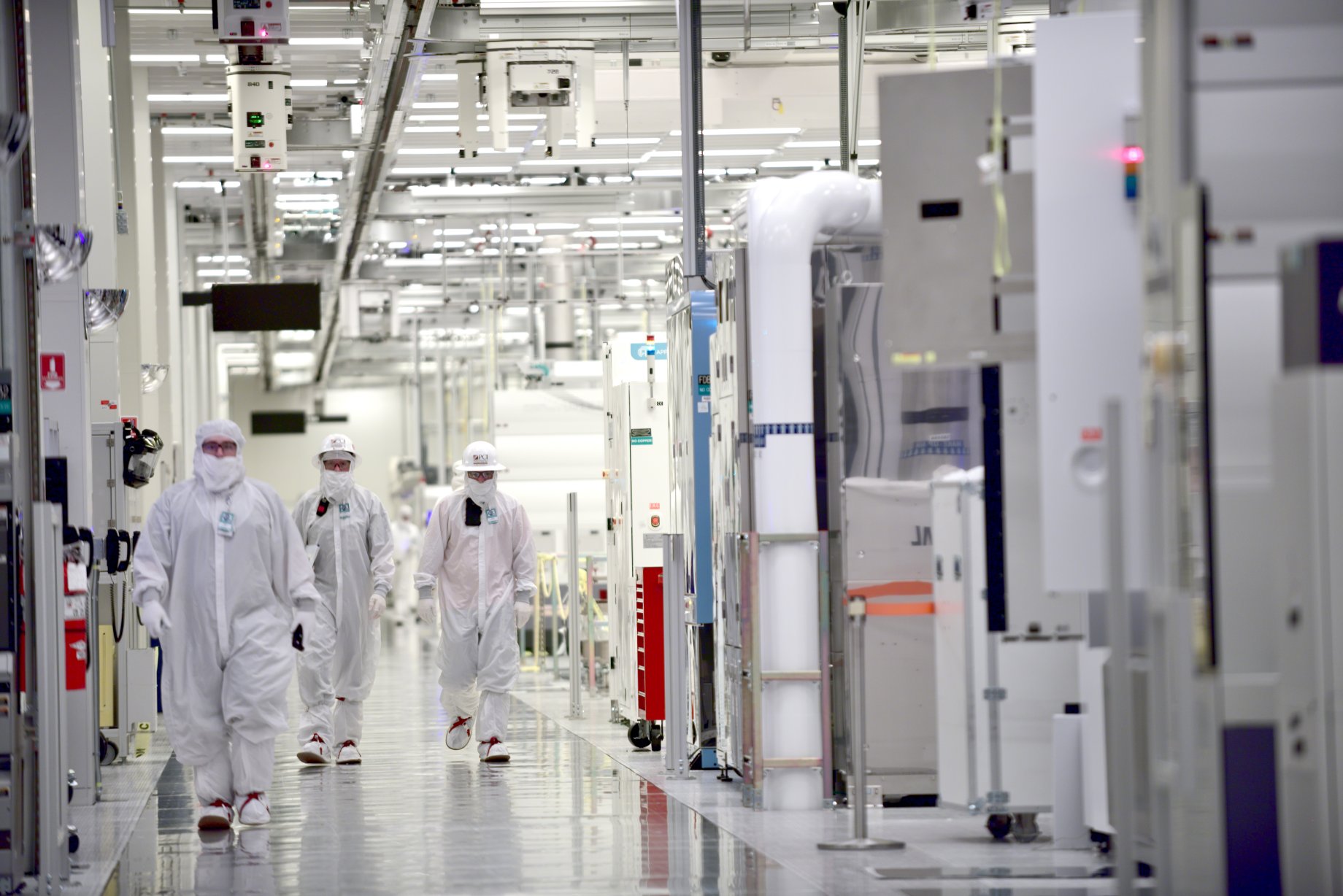 Intel employees wearing clean-room suits at a manufacturing plant.