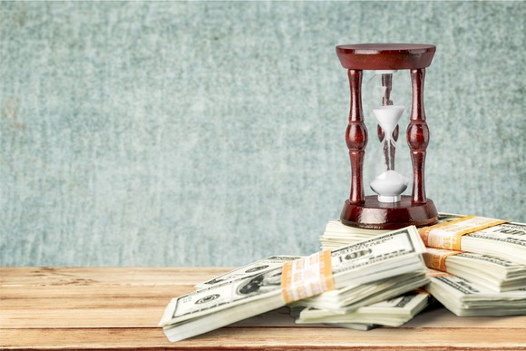 Stacks Of bills piled up near an hourglass