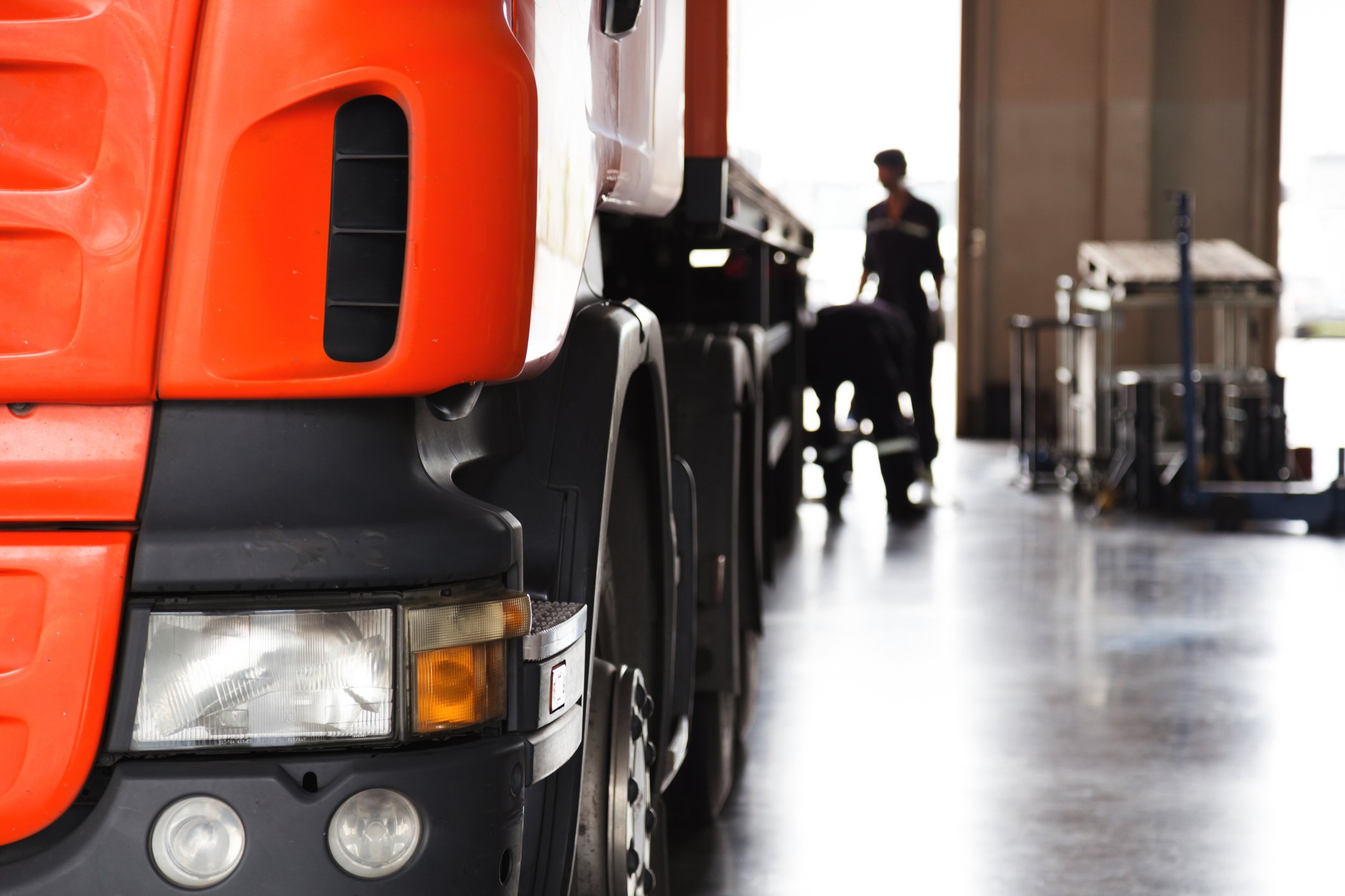 Vehicle mechanic inspecting semi-truck in large maintenance garage.