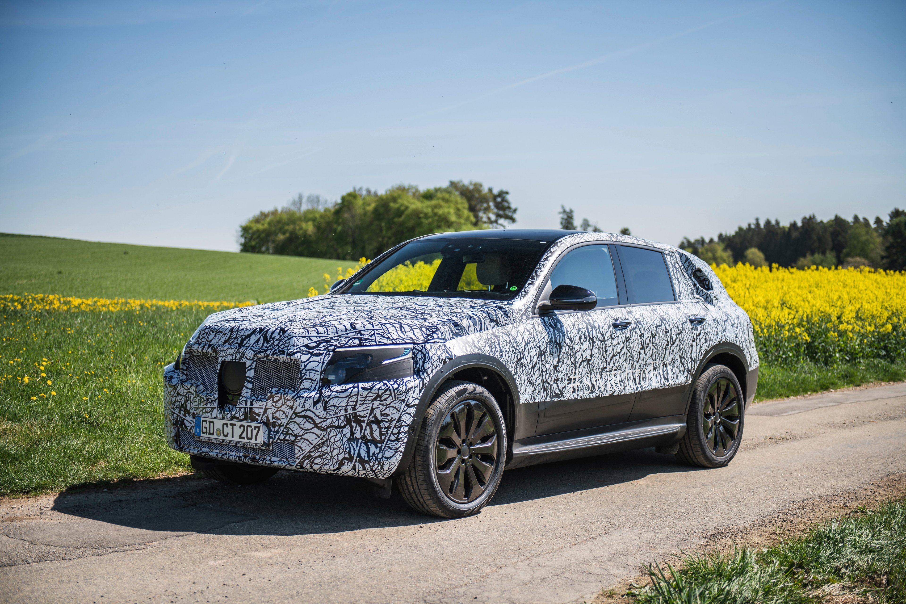 The Mercedes-Benz EQA, a compact electric SUV, shown wrapped in black and white camouflage and parked next to a field.