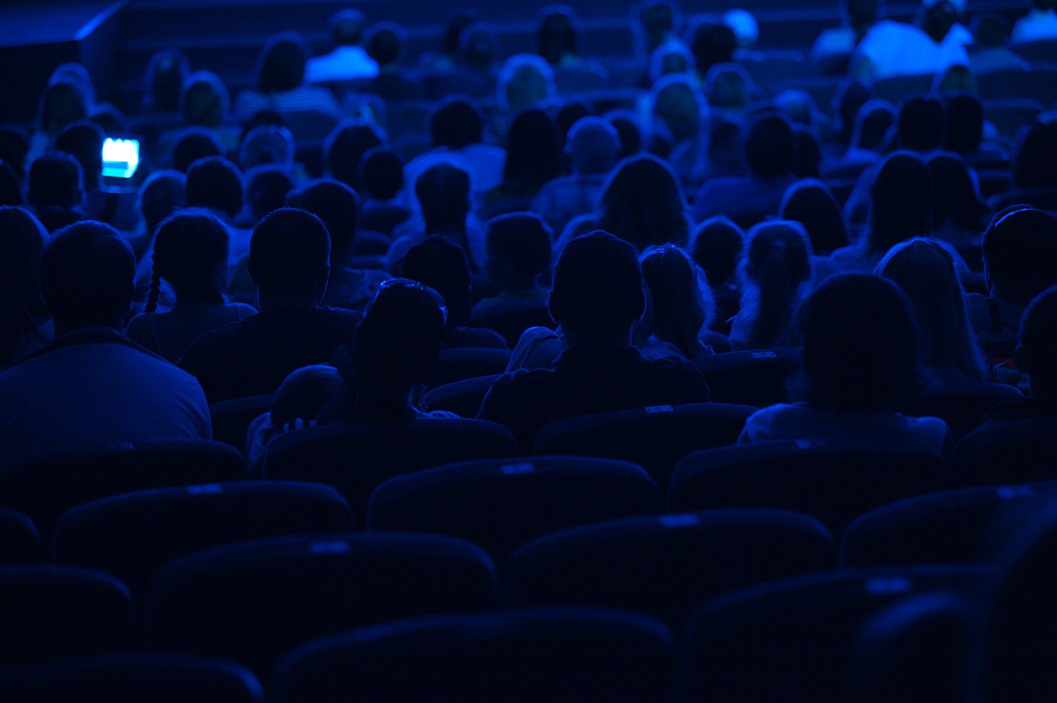 Movie-goers in darkened theater shown from behind.