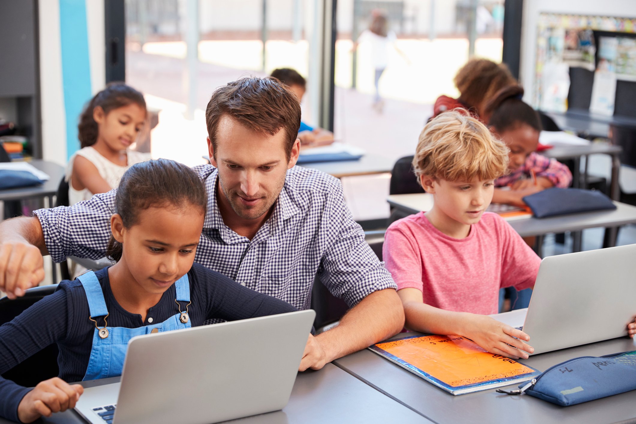 A man looks on as students use computers in a classroom.