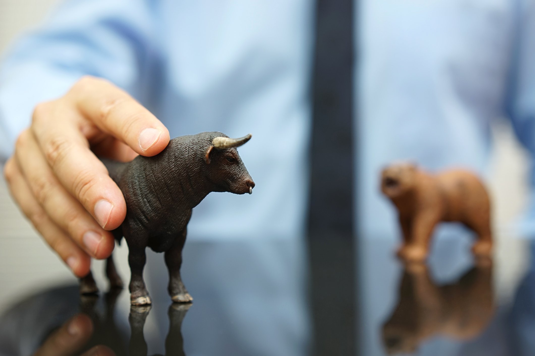 Businessman with his hand on a toy bull on a table with a toy bear also on the table