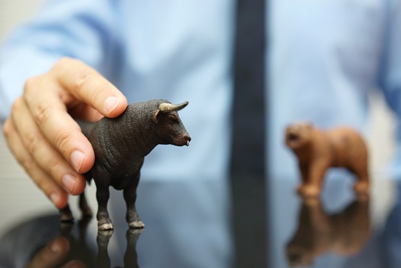 Businessman with his hand on a toy bull on a table with a toy bear also on the table