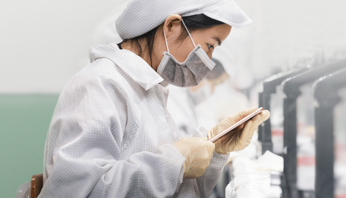 Chinese worker in a clean suit inspecting an iPhone