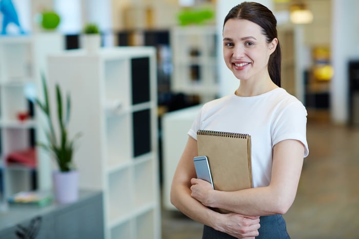 Young female in an office holding a note pad and a smartphone.