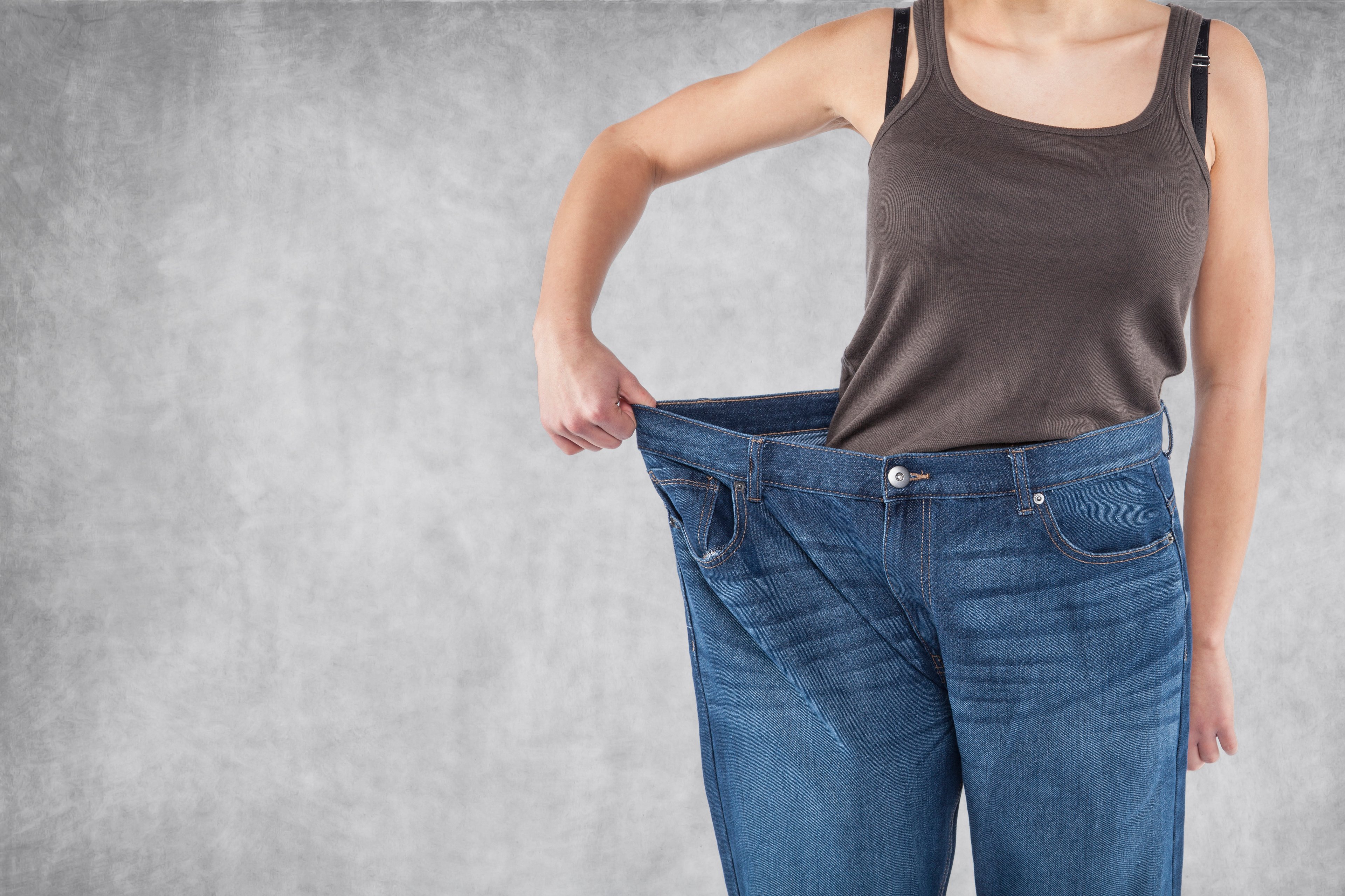 A person holding out the waist of their jeans to show that the jeans are too big for them.