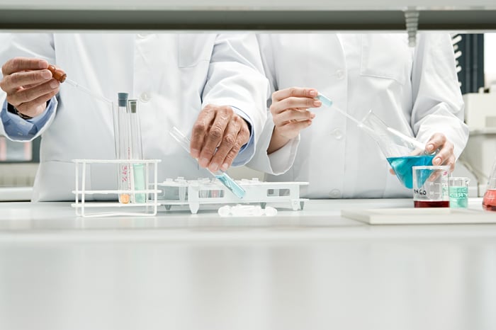 Two scientists standing side by side in lab with test tubes and beakers in front of them