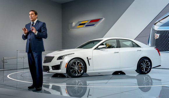 Reuss is shown standing on an auto-show stage with a while Cadillac CTS-V, a midsize high-performance luxury sedan. 