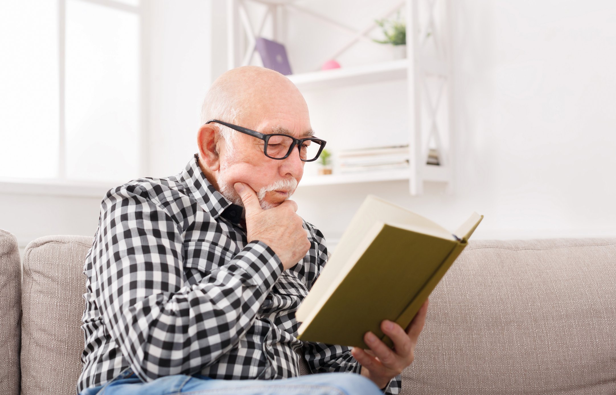 Senior man reading a book on a couch.