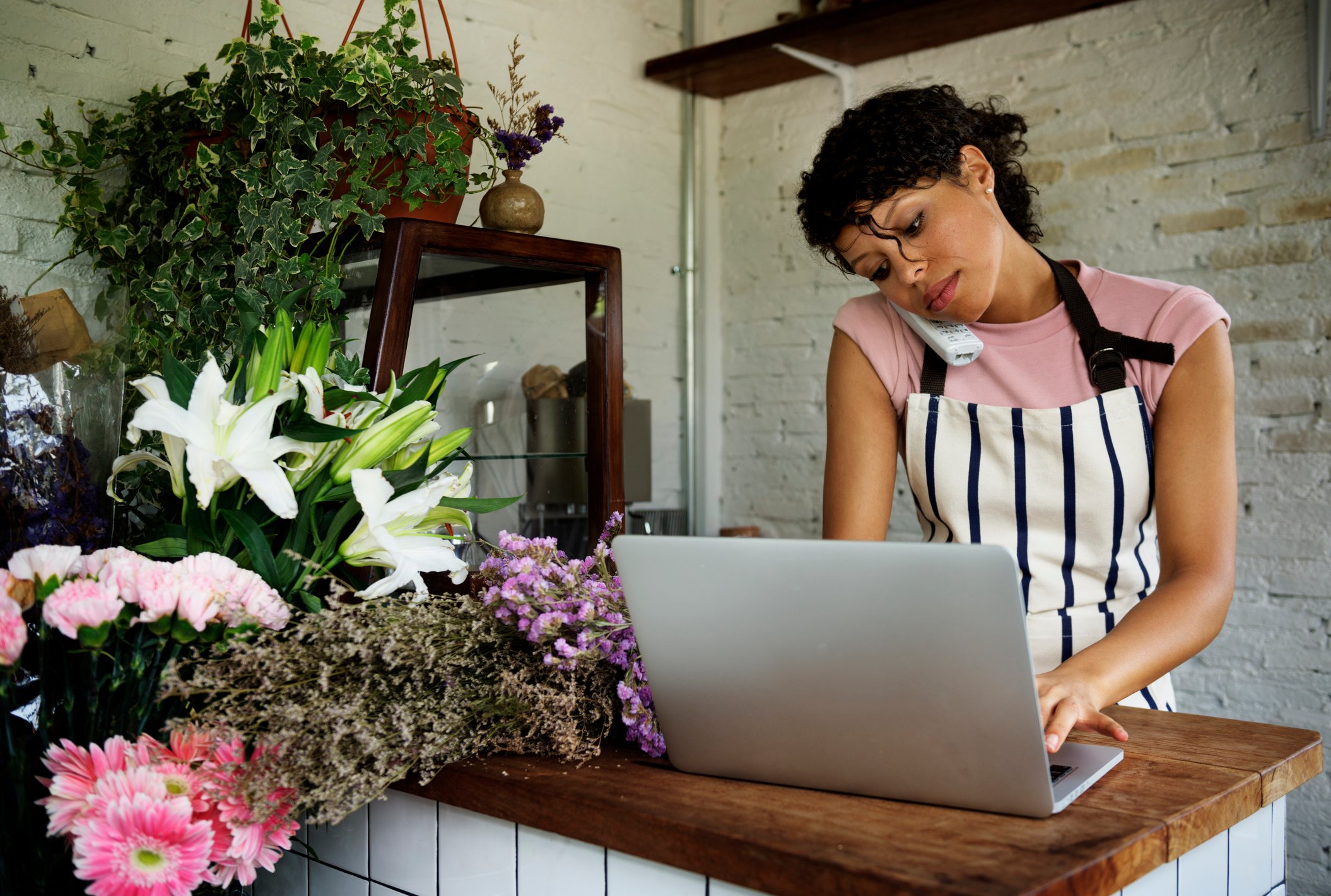 Woman using a laptop while on the phone in a flower shop