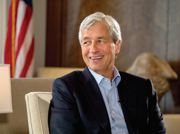 Jamie Dimon smiling while sitting on a beige chair.