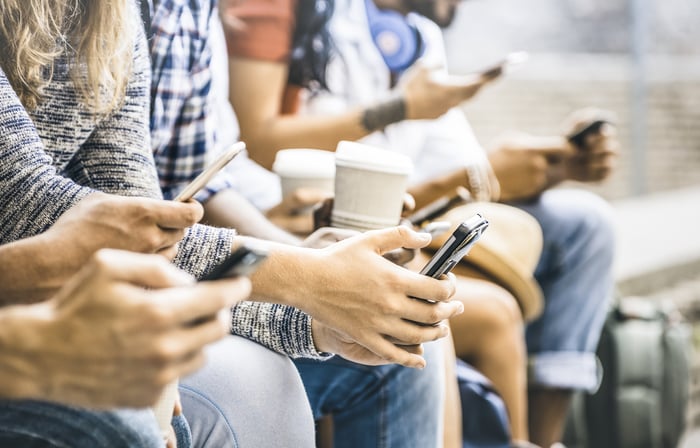 People sitting on bench looking at their cell phones. 