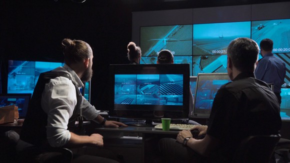 A special forces and policemen surveillance team in a modern office with large live screens.