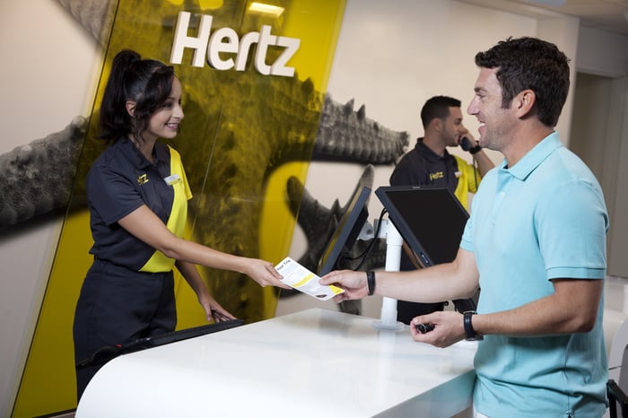 Customer getting a document from an employee behind the counter, with a Hertz logo behind them.