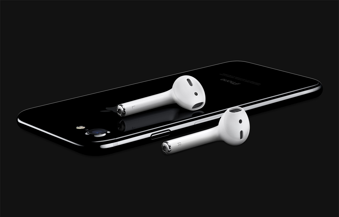 White AirPods laying on a black iPhone against a black background.