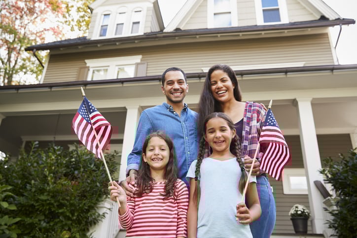 A family on the front porch of their home waving American flags.